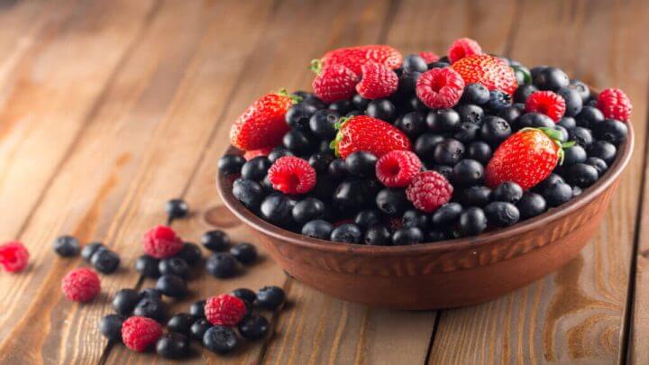 Vasilha de madeira com frutas vermelhas. Morangos, framboesas e mirtilos