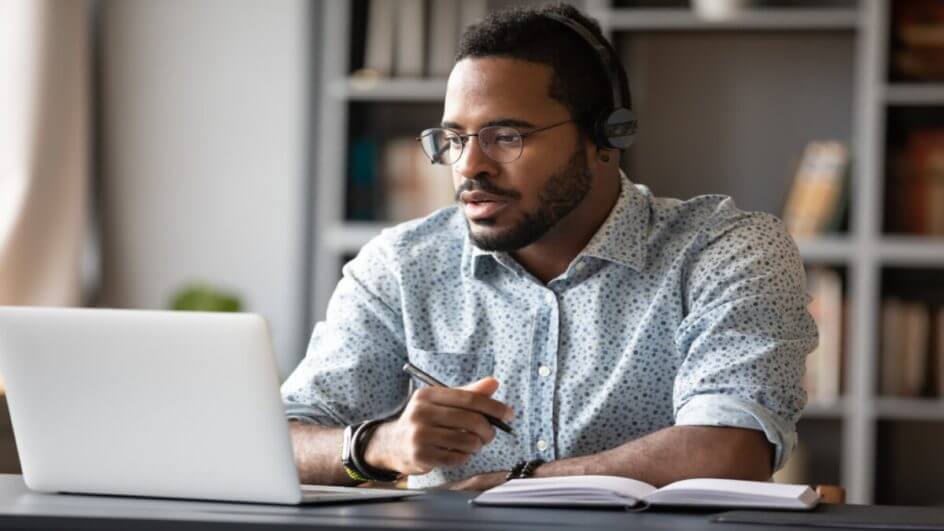 Homem de fone em frente a um notebook estudando