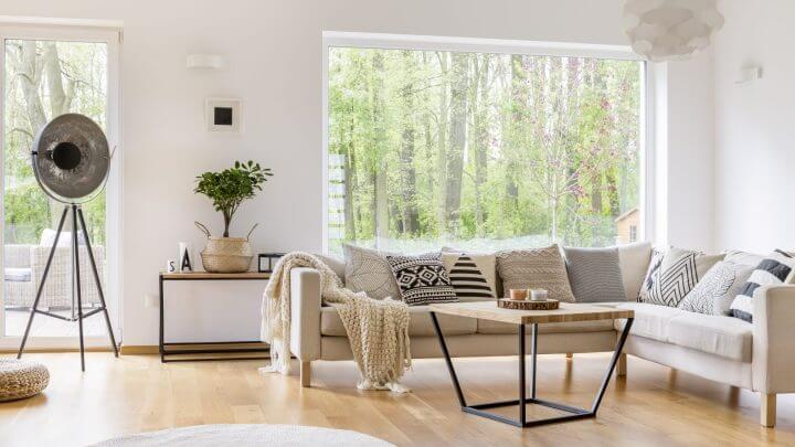 Sala de estar com janela ao fundo, sofá branco e mesa de centro de madeira