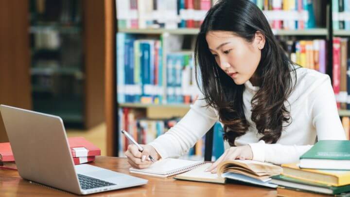 Garota estudando na biblioteca do colégio com livros e notebook