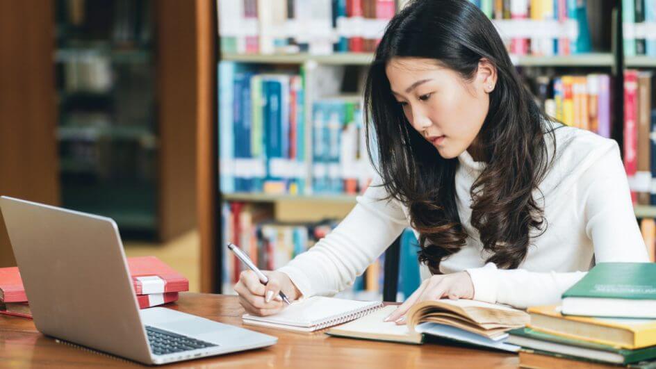Garota estudando na biblioteca do colégio com livros e notebook