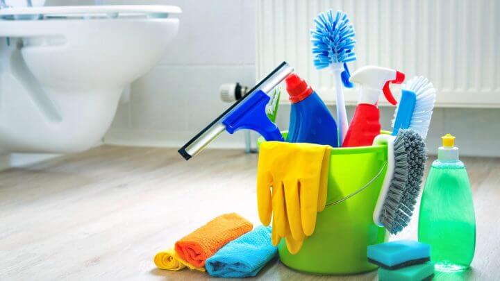 Produtos de limpeza em um balde verde no chão do banheiro