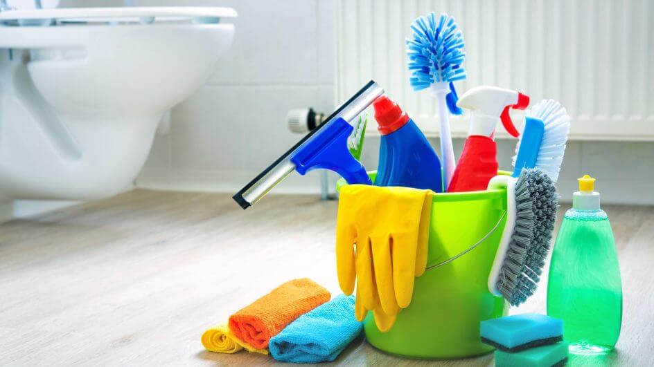Produtos de limpeza em um balde verde no chão do banheiro