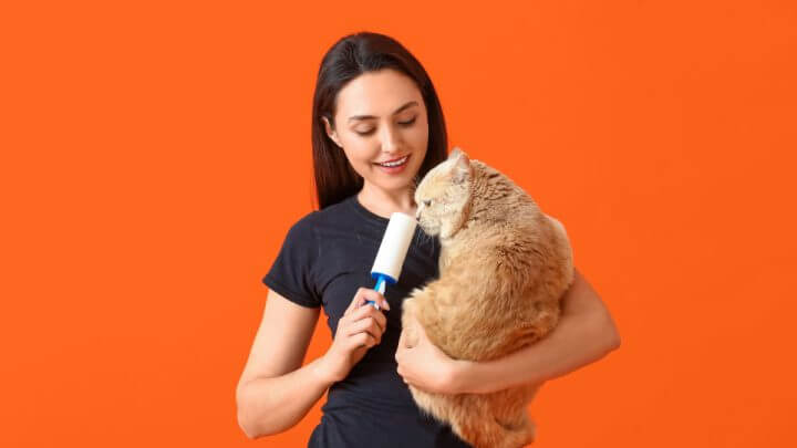 Mulher de roupa preta com gato laranja no colo e rolo para remoção de pelos