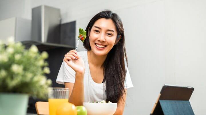 Mulher sorrindo segurando um garfo com salada