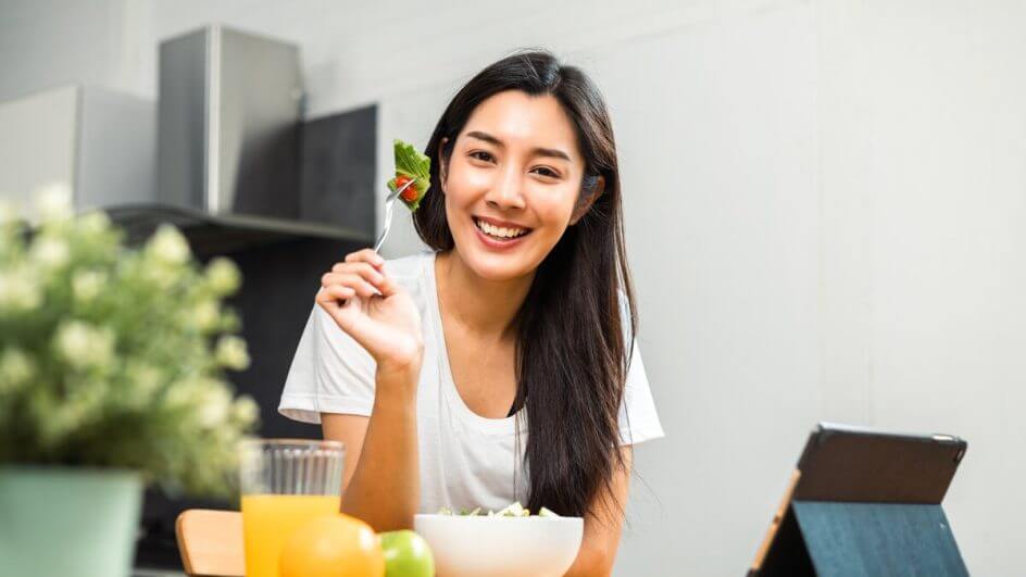 Mulher sorrindo segurando um garfo com salada