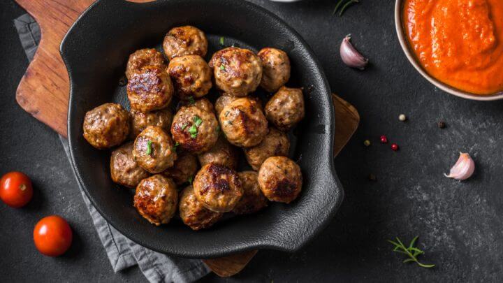 Almondegas de carne moída em recipiente preto com molho vermelho ao lado