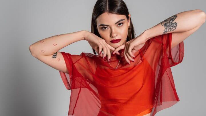 Mulher com as duas mãos no queijo vestindo blusa vermelha transparente