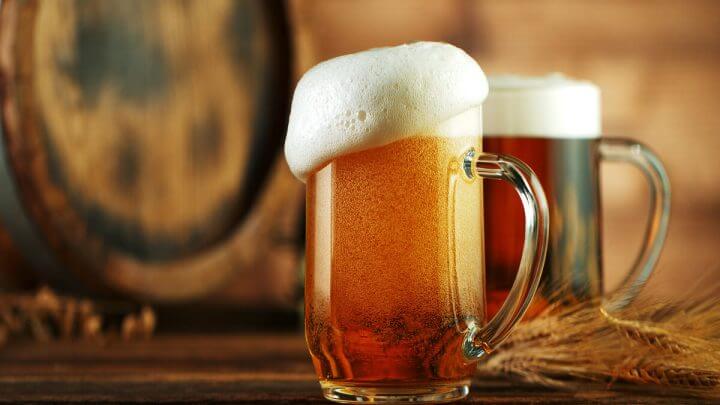 Duas canecas com cerveja em cima de uma mesa de madeira