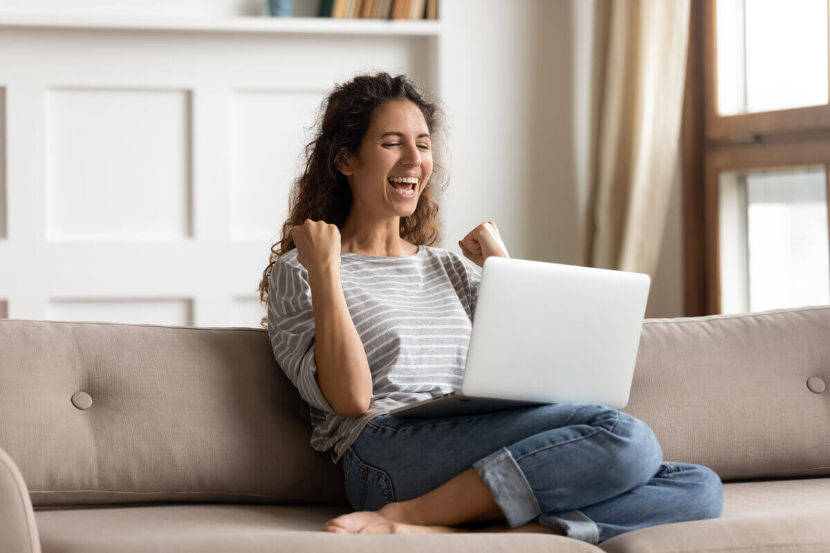 Mulher feliz sentada em um sofá com um notebook em cima da perna