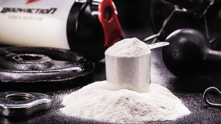 Recipiente branco com creatina em cima de uma mesa preta ao lado de uma garrafa