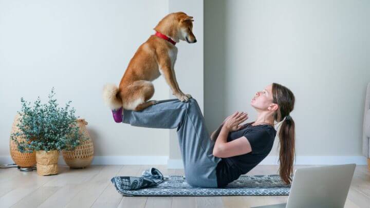 Jovem mulher em posição de ioga equilibrando com seu cachorro.