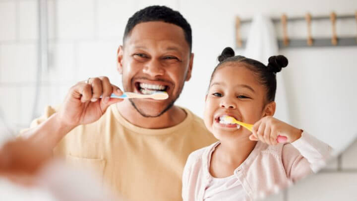 Pai e filha escovando os dentes em frente ao espelho