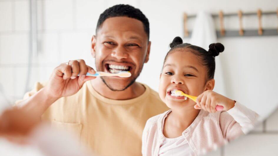 Pai e filha escovando os dentes em frente ao espelho
