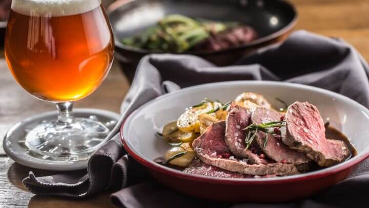 Filé Mignon fatiado servido com batata em prato, ao lado de cerveja.