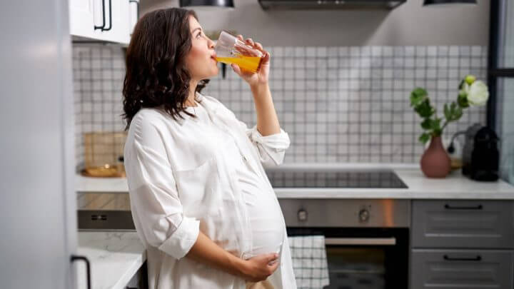 Mulher grávida tomando suco de laranja na cozinha de casa