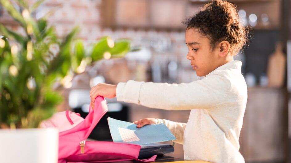 Menina guardando livros em uma mochila rosa