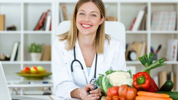 Médica sentada em frente a uma mesa com legumes