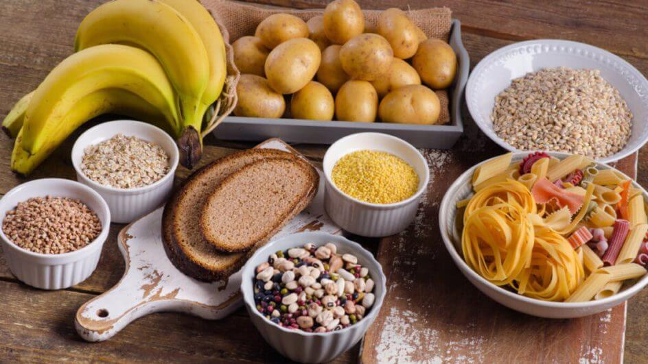 Mesa de madeira com banana, batatas, pão e prato com macarrão