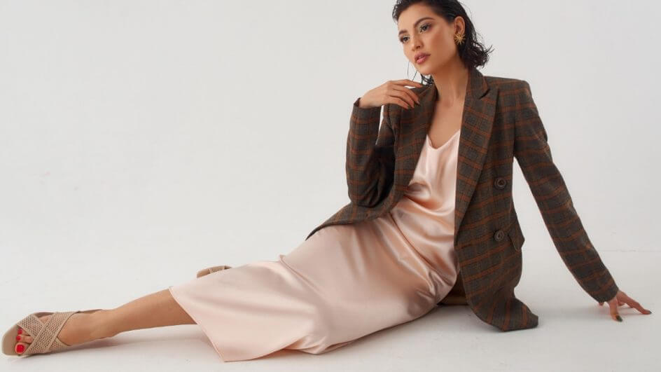 Modelo sentada vestindo um slip dress com blazer em um fundo branco