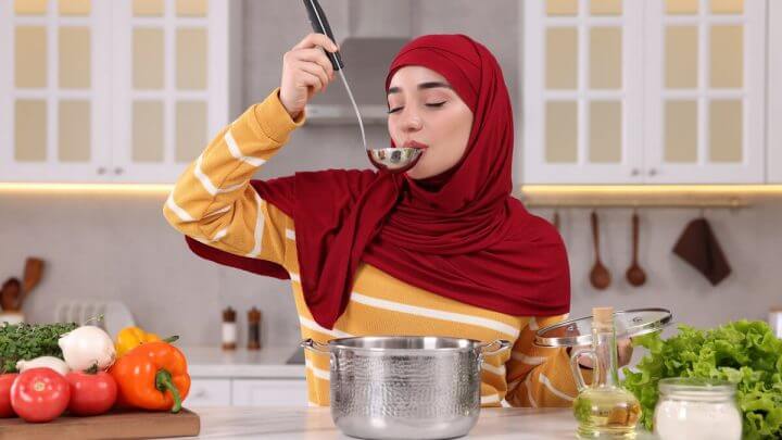 Mulher em uma cozinha com concha na boca e segurando uma panela