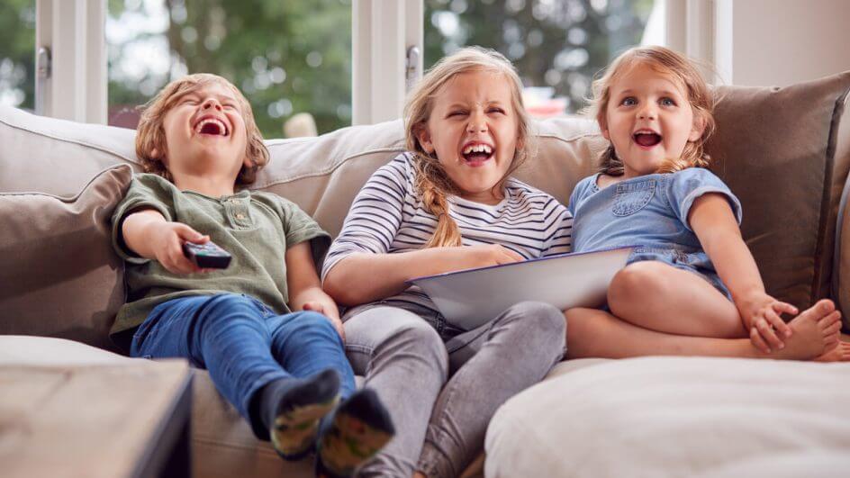 Duas meninas e um menino sentados em um sofá assistindo à televisão