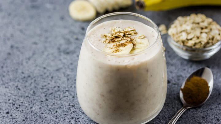 Copo de vidro com vitamina de banana decorada com rodelas de banana e canela em pó