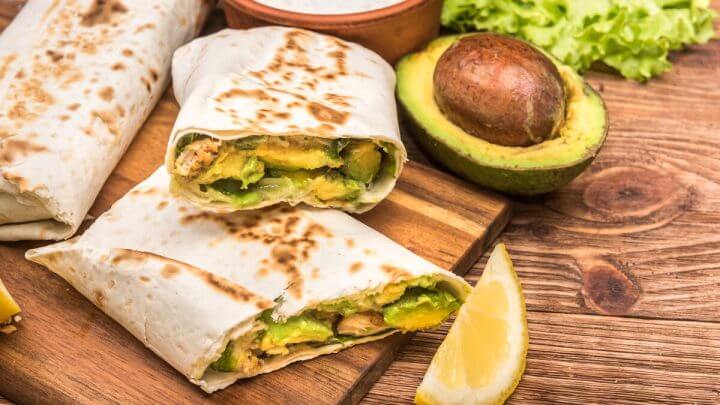 Wrap recheado com frango e abacate em cima de uma tábua de madeira