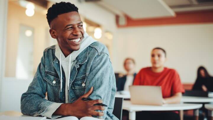 Estudante sentado na sala de aula da universidade olhando para longe e sorrindo