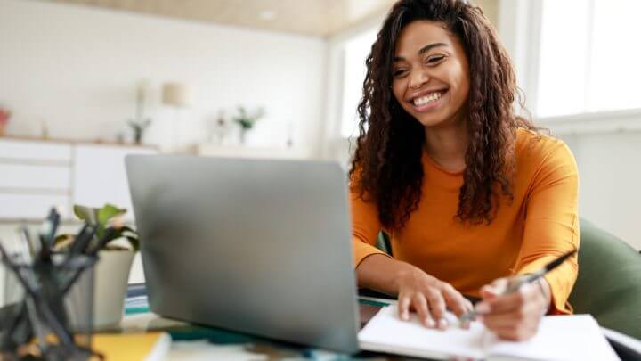 Estudante fazendo anotações no computador e caderno