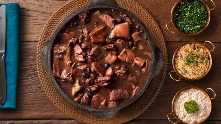 Feijoada completa com alguns acompanhamentos ao lado, como arroz, couve e farofa