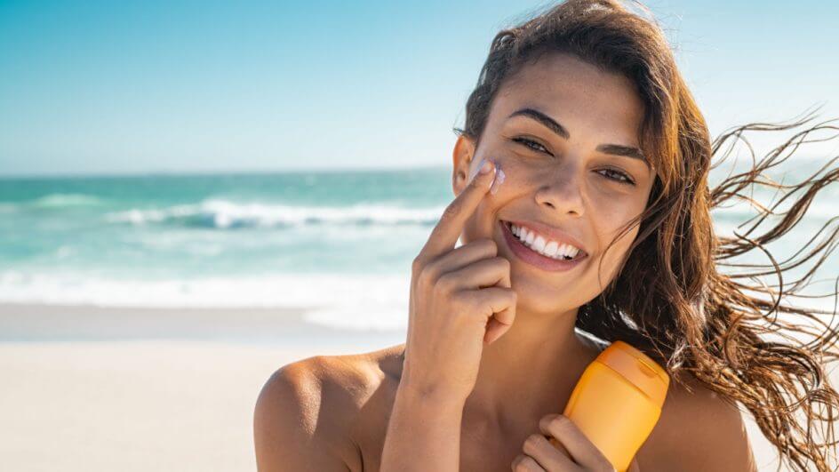 Mulher na praia passando protetor solar no rosto