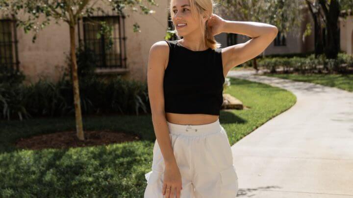 Mulher com camisa regata preta e calça branca em um jardim