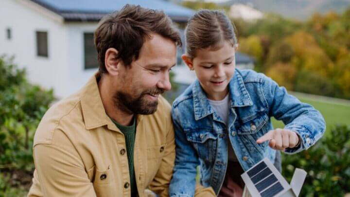 Menina com o pai segurando um modelo de papel de uma casa com painéis solares