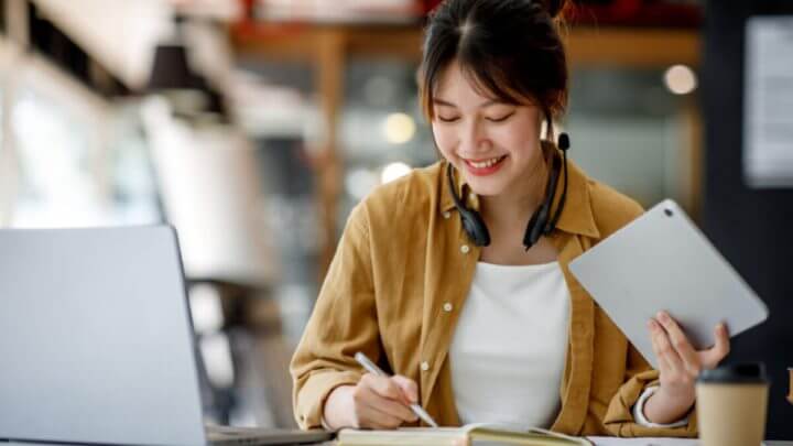 Mulher estudando com caderno, computador e tablet.