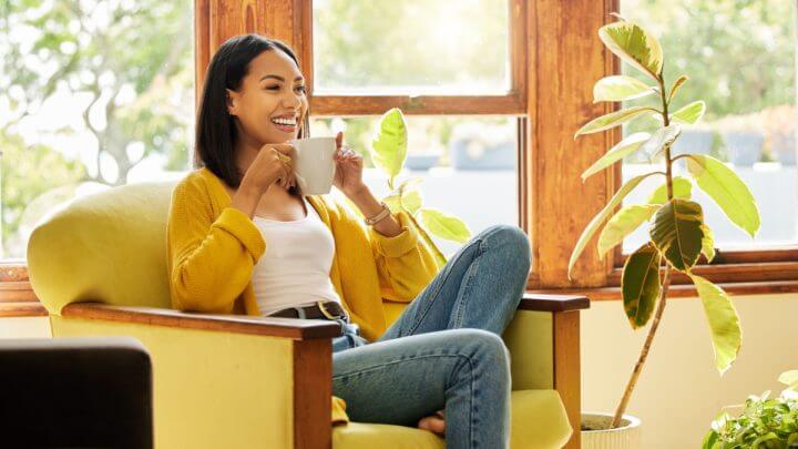 Mulher sorridente sentada em poltrona tomando café