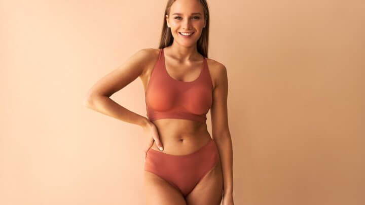 Mulher com lingerie bege com as mãos na cintura sorrindo