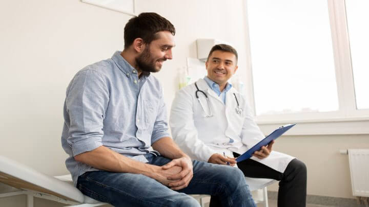 Homem em consulta médica; o paciente e o profissional estão sentados em maca.