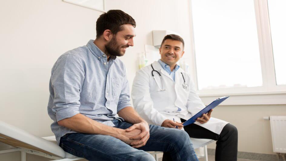 Homem em consulta médica; o paciente e o profissional estão sentados em maca.