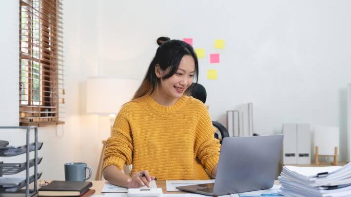Mulher vestindo blusa amarela e sorrindo mexendo em um notebook