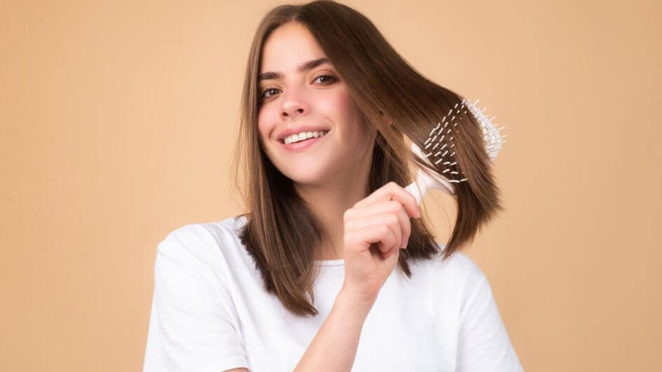 Mulher vestindo blusa branca e sorrindo penteando os cabelos