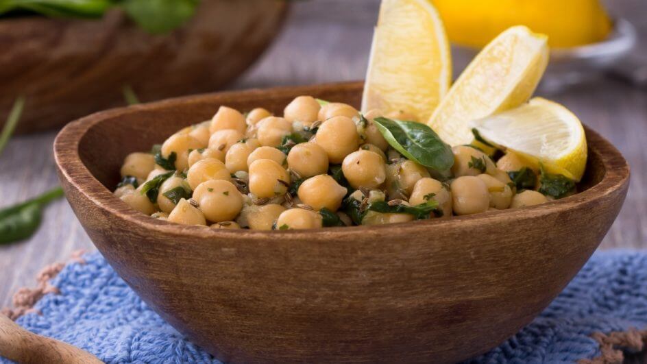 Recipiente de madeira com salada de grão-de-bico e espinafre decorado com rodelas de limão