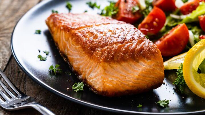 Posta de salmão em cima de um prato preto com salada