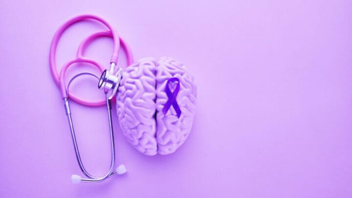 Objetos roxos como estetoscópio, cérebro e faixa para representar o mês de conscientização do Alzheimer