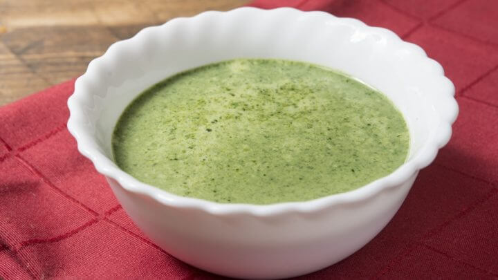 Recipiente branco com sopa de abacate em cima de uma mesa de madeira com pano vermelho