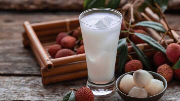 Copo de vidro com suco de lichia com gelo em cima de uma mesa de madeira