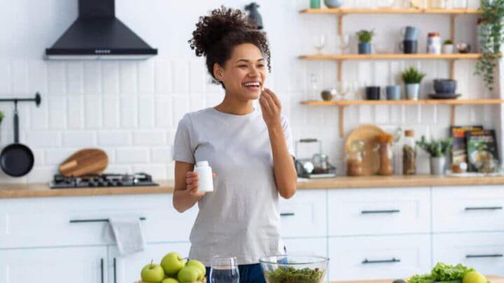 Mulher em cozinha tomando comprimido de suplemento alimentar