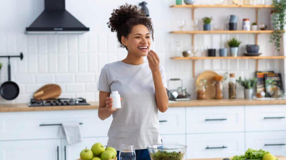 Mulher em cozinha tomando comprimido de suplemento alimentar