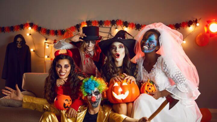 Jovens alegres vestidos de bruxa maluca, demônio, vampiro, noiva cadáver e palhaço com machado se divertindo juntos na festa de Halloween