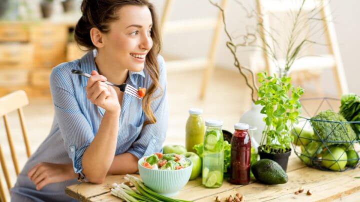 Mulher sentada na mesa comendo salada com ingredientes frescos verdes